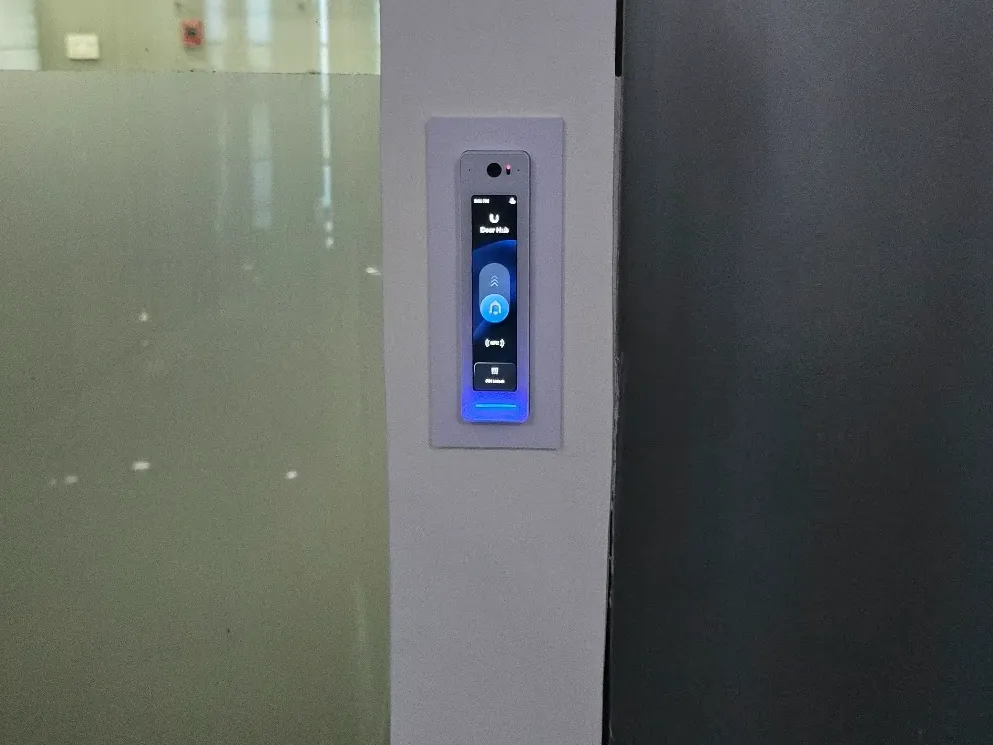 Lector de control de acceso con pantalla táctil y cámara, instalado en el marco de una puerta de oficina