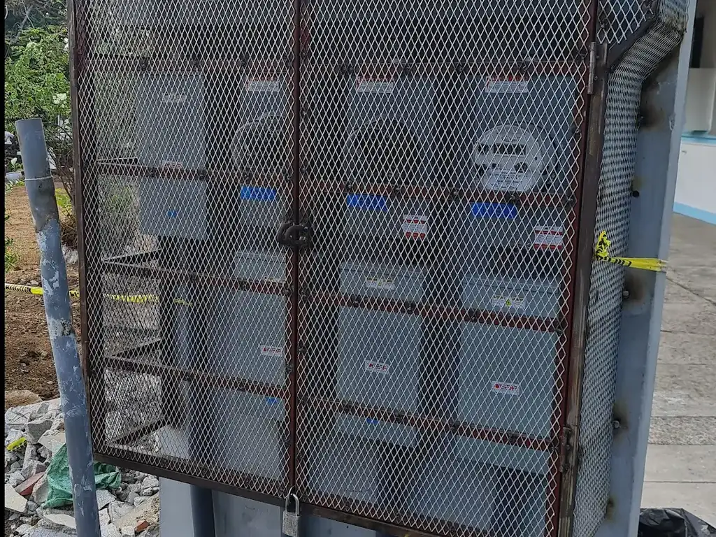 Gabinete exterior de medidores eléctricos protegido con malla metálica y candado