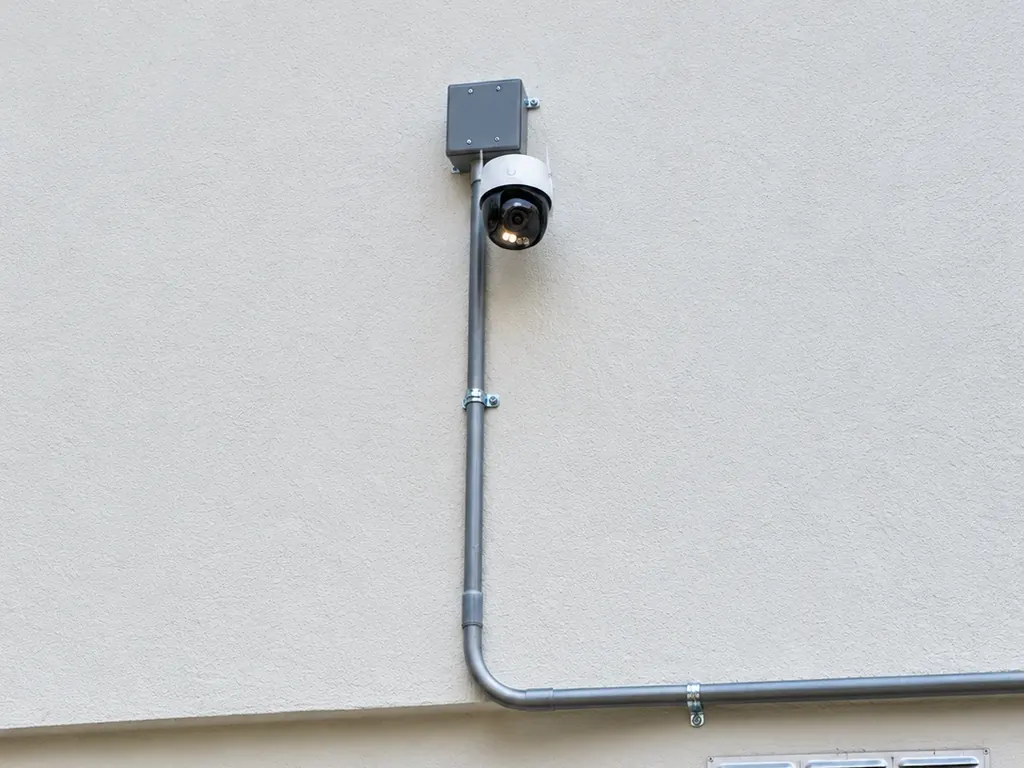 Cámara de seguridad tipo domo instalada en la fachada de una casa, con caja de conexiones y tubería ordenada