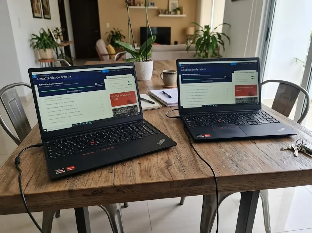 Dos laptops nuevas encendidas y configuradas sobre una mesa de comedor de madera, en una casa